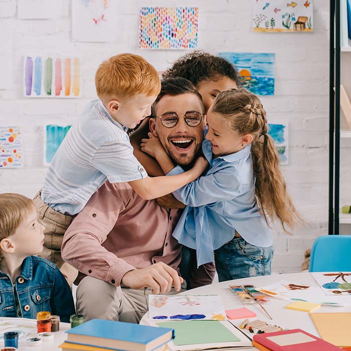 Male teacher in a classroom with kids hugging him